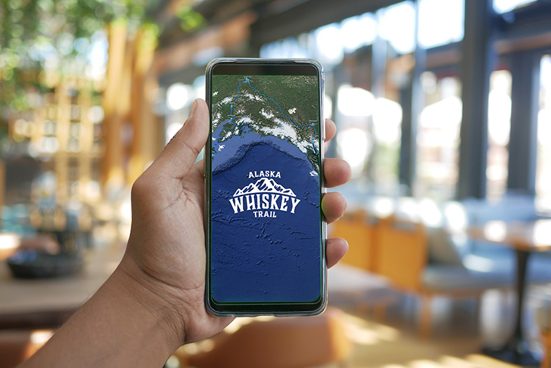 young man hand using smart phone with green screen at cafe Anchorage Distillery bottle
